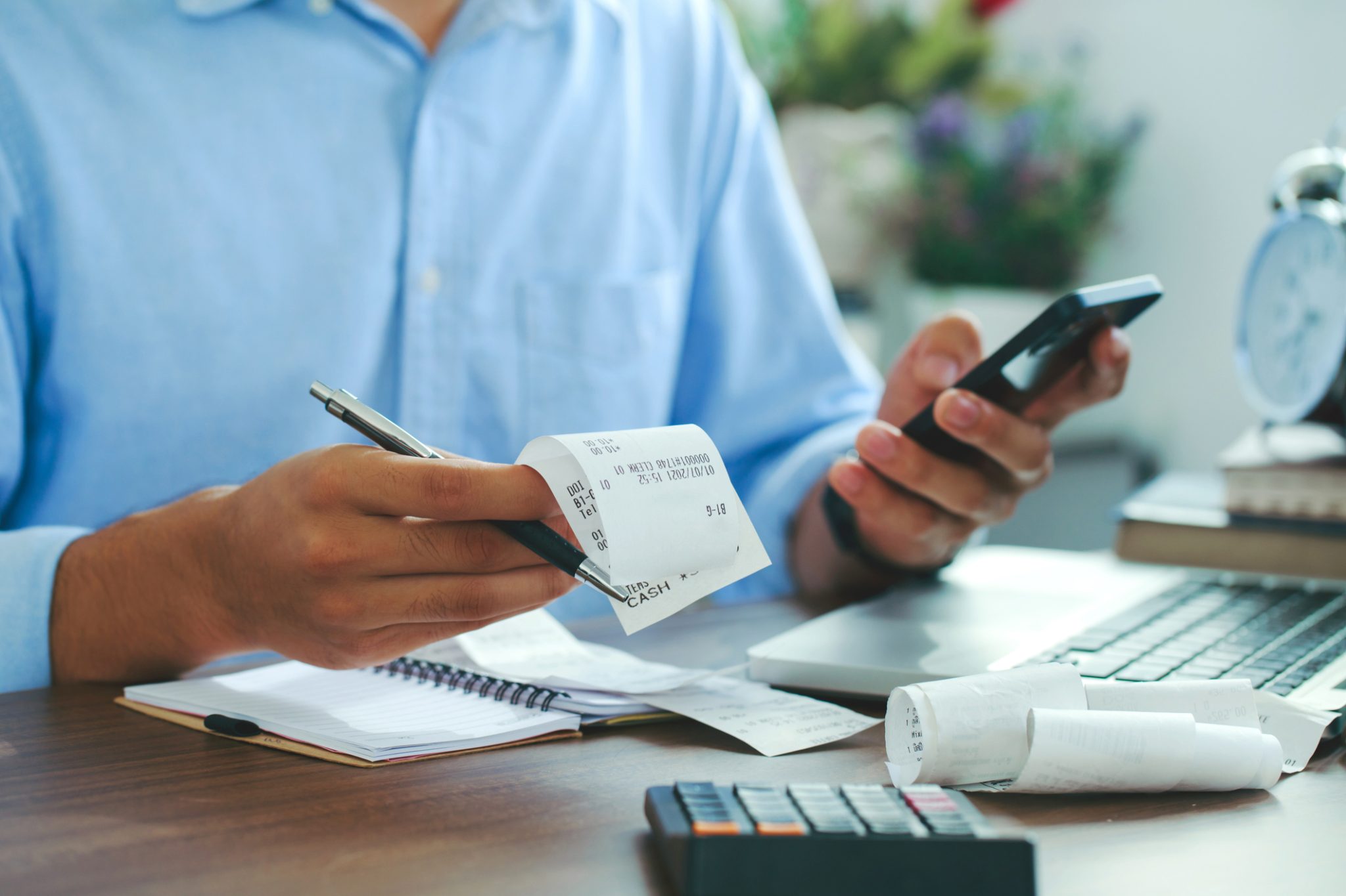 An adult in a blue shirt with receipts and calculators sits at a desk trying to file tax credits and rebates for heat pumps under the Inflation Reduction Act.