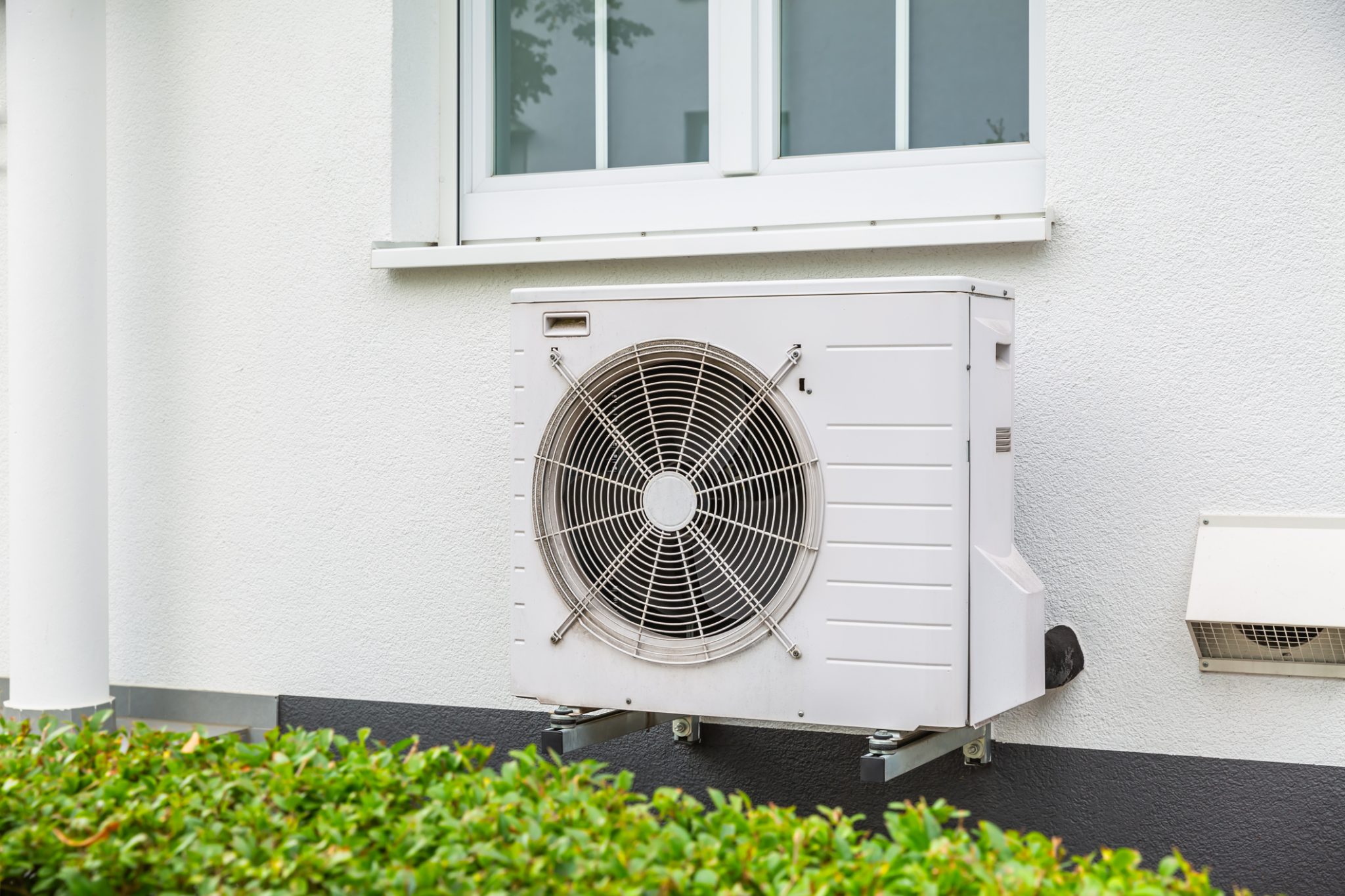 A white mini-split heat pump installed outside of a house underneath a double window.