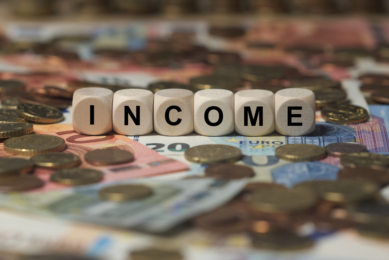 Wooden blocks spelling out the word “income” surrounded by money from different countries.