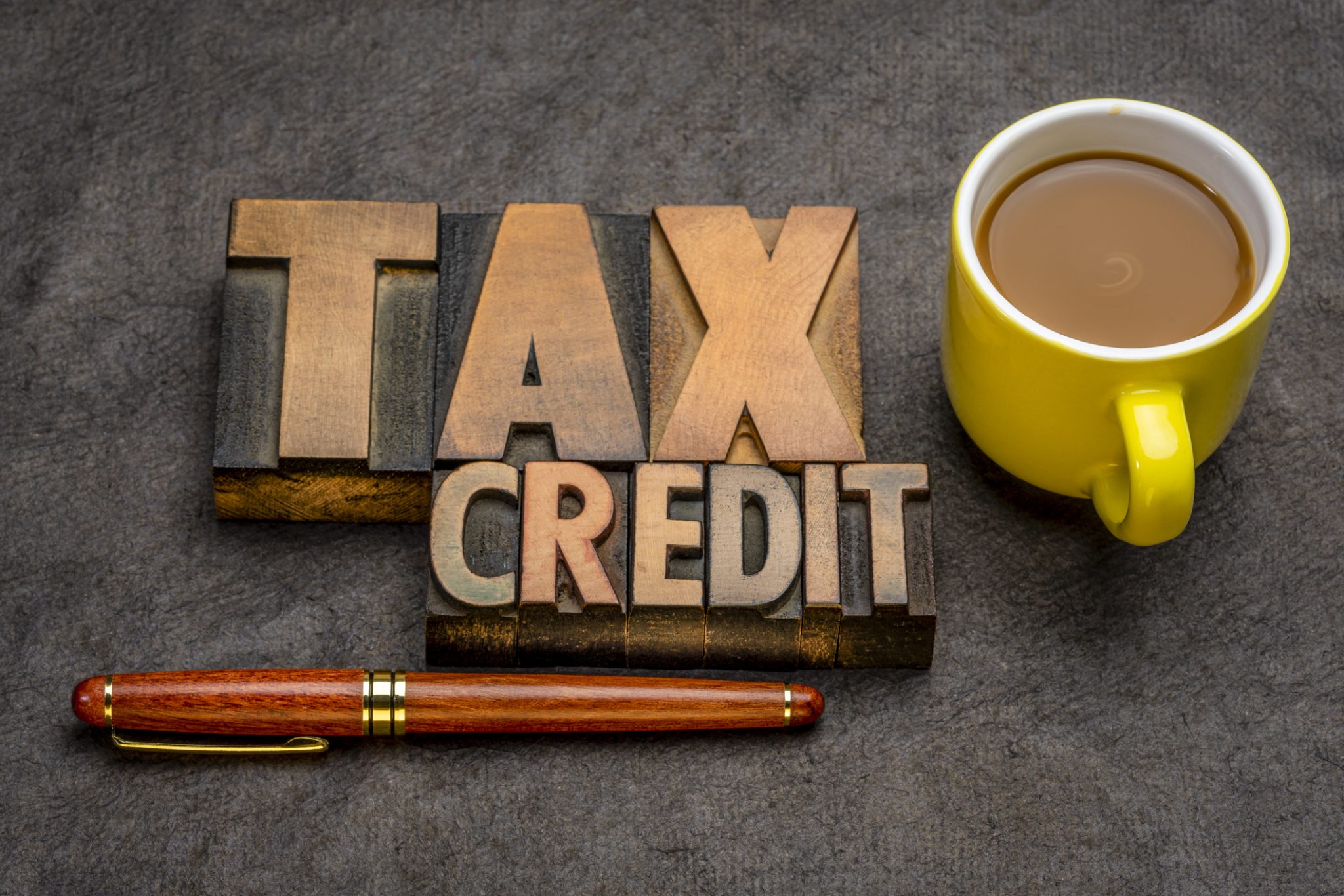 Wooden blocks with the words “tax credit” next to a cup of coffee and a pen, signifying information on the 25C tax credit.