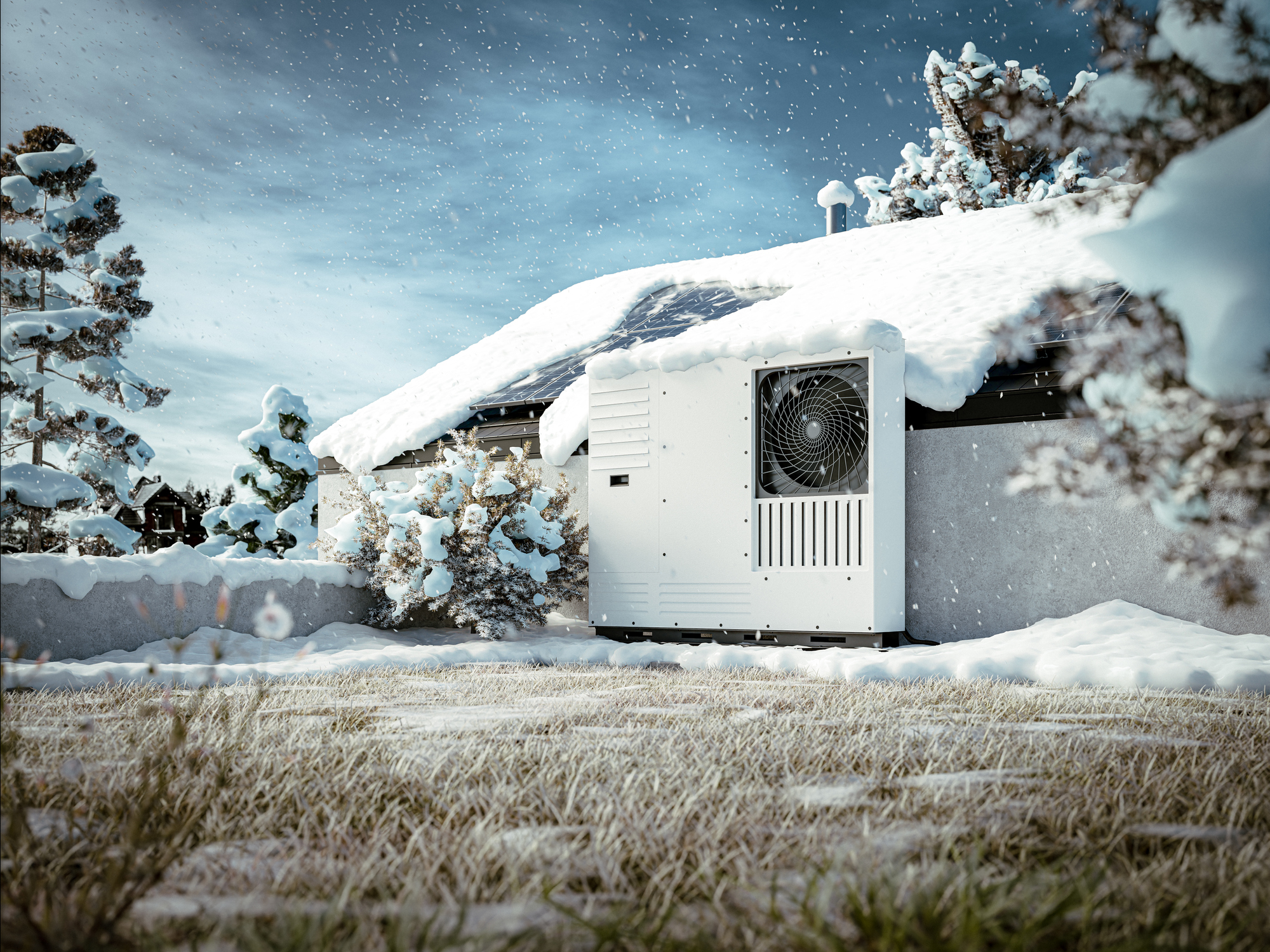 A cold climate heat pump installed on the side of a house with snow on the roof and frost-covered grass.