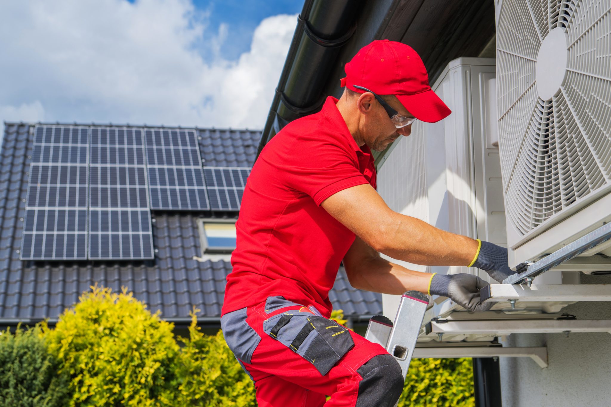 A licensed heat pump installer performing installation of a new heat pump on a home with solar panels.